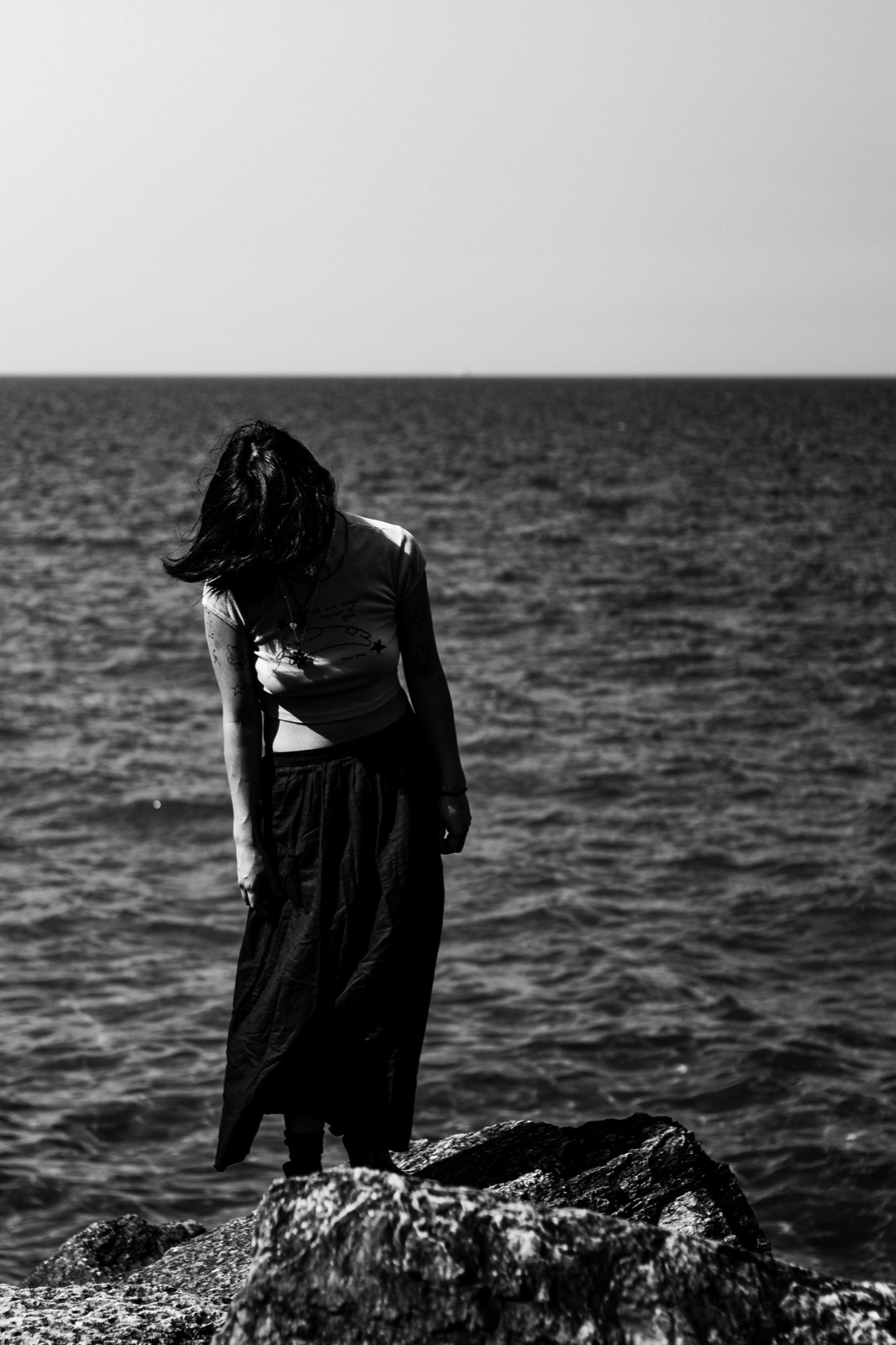 Black and white portrait on lakefront rocks, hair windblown across the face