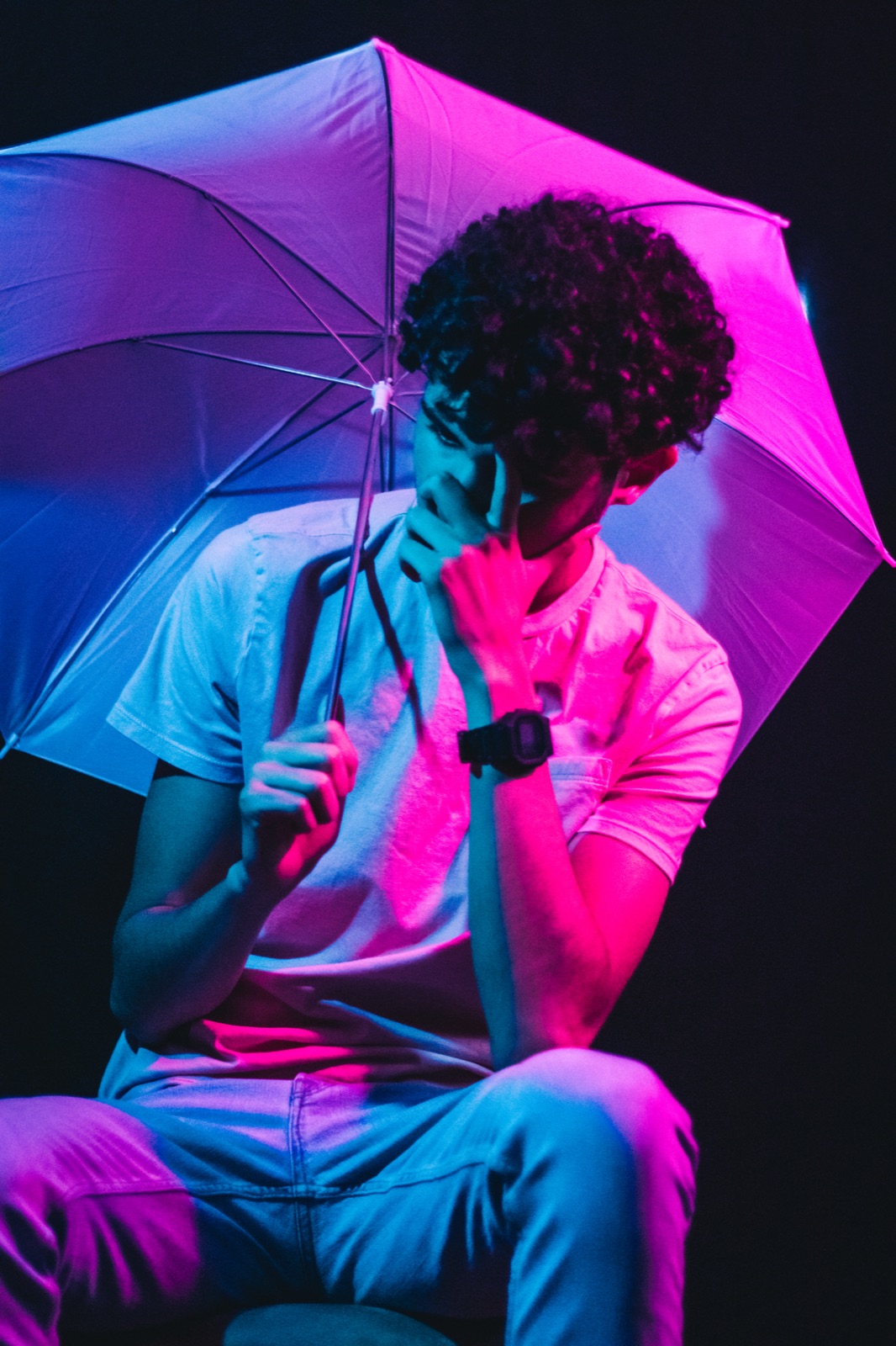 Neon-lit studio portrait, seated beneath an umbrella