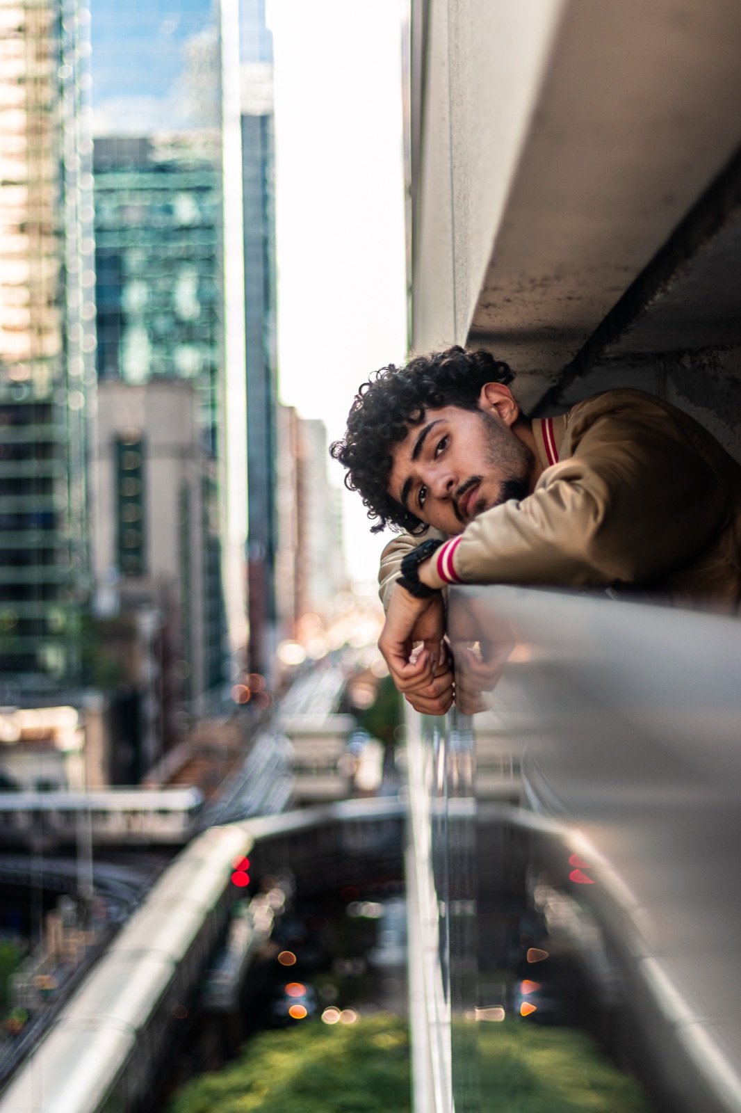 Portrait resting on a glass railing above downtown train tracks